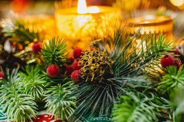 Yeşil ladin dalları arasında üç mum ve ışık ve altın külahlı kırmızı buzlu böğürtlenlerle güzel bir yeni yıl mumu tutucusu. Sıcak ve rahat dekorasyon.