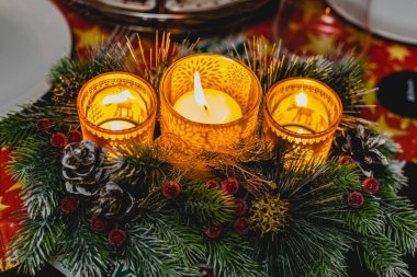 Yeşil ladin dalları arasında üç mum ve ışık ve altın külahlı kırmızı buzlu böğürtlenlerle güzel bir yeni yıl mumu tutucusu. Sıcak ve rahat dekorasyon.