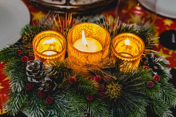 Yeşil ladin dalları arasında üç mum ve ışık ve altın külahlı kırmızı buzlu böğürtlenlerle güzel bir yeni yıl mumu tutucusu. Sıcak ve rahat dekorasyon.