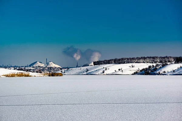 High and wide chimney, a pipe with a large amount of smoke and substances released into the atmosphere. Part of a factory or enterprise that pollutes the environment in a snowy and frosty winter near the city