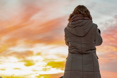 Kameralı bir kız, bulutlu bir gökyüzünde, bulutlu bir akşam günbatımını çekiyor. Açık havada karanlık aydınlıkta, güzel bir parıltı manzarası olan fotoğrafçının silueti.