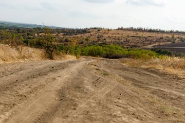 Kuru bitki örtüsü ve çimenlerin arasında toz toprak ve kum dönüşleriyle dolambaçlı geniş bir yol. Güzel bulutlu bir gökyüzünün arka planında. Sarı kuruyan bitkiler ve çalılar