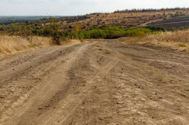 Kuru bitki örtüsü ve çimenlerin arasında toz toprak ve kum dönüşleriyle dolambaçlı geniş bir yol. Güzel bulutlu bir gökyüzünün arka planında. Sarı kuruyan bitkiler ve çalılar