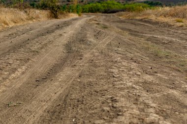 Kuru bitki örtüsü ve çimenlerin arasında toz toprak ve kum dönüşleriyle dolambaçlı geniş bir yol. Güzel bulutlu bir gökyüzünün arka planında. Sarı kuruyan bitkiler ve çalılar