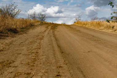 Kuru bitki örtüsü ve çimenlerin arasında toz toprak ve kum dönüşleriyle dolambaçlı geniş bir yol. Güzel bulutlu bir gökyüzünün arka planında. Sarı kuruyan bitkiler ve çalılar