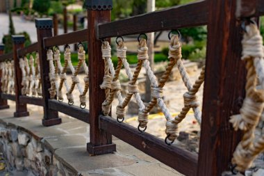 Kalın ipler, çapraz sarmaş dolaş, ahşap korkuluklara tutun, eğlence için Park 'taki ara sokak boyunca dekoratif çitlere asılın. Metal halkalar ve taştan bir zemin üzerinde büyük güçlü düğümler.