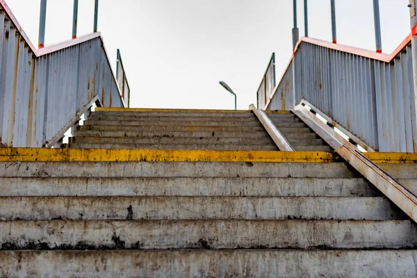 Dirty, trampled concrete steps with metal railings on each side. Old built structure for walking. Ascent and descent in the open air on the street.