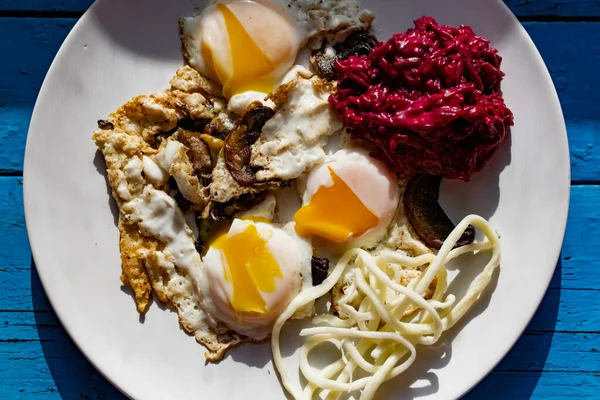 Fried eggs with mushrooms, long cheese noodles and beetroot caviar, a hearty fried dish for Breakfast with appetizers. The flowing liquid yellow egg yolk — Stock Image Fried Eggs Mushrooms Long Cheese Noodles Beetroot Caviar Hearty Fried Royalty Free Stock Photos