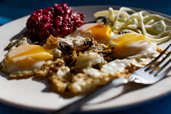 Fried eggs with mushrooms, long cheese noodles and beetroot caviar, a hearty fried dish for Breakfast with appetizers. The flowing liquid yellow egg yolk — Stock Image Fried Eggs Mushrooms Long Cheese Noodles Beetroot Caviar Hearty Fried Stock Picture
