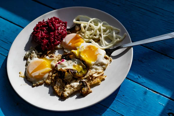 Fried eggs with mushrooms, long cheese noodles and beetroot caviar, a hearty fried dish for Breakfast with appetizers. The flowing liquid yellow egg yolk — Stock Image Fried Eggs Mushrooms Long Cheese Noodles Beetroot Caviar Hearty Fried Royalty Free Stock Images