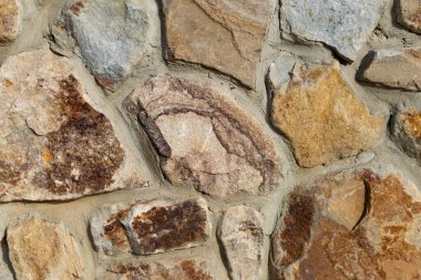Düz taşlar ve çimento arka planı, doğal malzemelerden yapılmış dekoratif duvar. Değişik boyutlarda ve şekillerde kumlu renklerden oluşan taşlı sert yüzey.