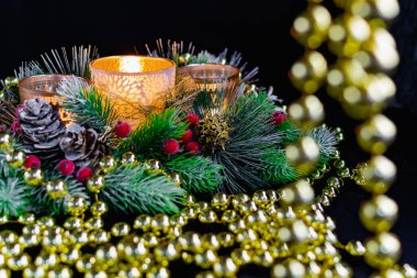 Mum ışığında siyah arka planda Noel süslemeleri. Altın toplar ve boncuklar, Noel ağacının desenleri ve dallarıyla açılan şamdanlar. Şenlikli sunumda zarif koniler ve kırmızı böğürtlenler