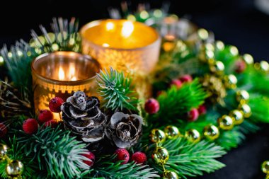 Mum ışığında siyah arka planda Noel süslemeleri. Altın toplar ve boncuklar, Noel ağacının desenleri ve dallarıyla açılan şamdanlar. Şenlikli sunumda zarif koniler ve kırmızı böğürtlenler