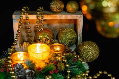 Mum ışığında siyah arka planda Noel süslemeleri. Altın toplar ve boncuklar, Noel ağacının desenleri ve dallarıyla açılan şamdanlar. Şenlikli sunumda zarif koniler ve kırmızı böğürtlenler