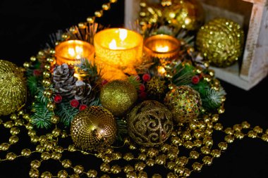 Mum ışığında siyah arka planda Noel süslemeleri. Altın toplar ve boncuklar, Noel ağacının desenleri ve dallarıyla açılan şamdanlar. Şenlikli sunumda zarif koniler ve kırmızı böğürtlenler