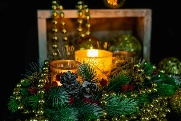 Mum ışığında siyah arka planda Noel süslemeleri. Altın toplar ve boncuklar, Noel ağacının desenleri ve dallarıyla açılan şamdanlar. Şenlikli sunumda zarif koniler ve kırmızı böğürtlenler