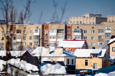 Plastik pencereli beyaz ve kırmızı tuğlalardan yapılmış çok katlı binalar, kışın soğuk, yemyeşil kar tabakasının altında durur..