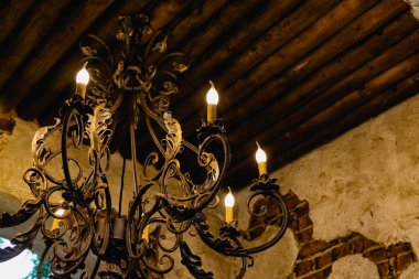 Mum ışığı şeklinde ampulleri olan antika bir avize, ahşap tavanda asılı gökyüzü manzaralı. Sahte süslemelerle metal açılış çerçevesi.