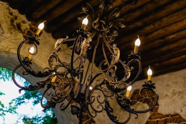 Mum ışığı şeklinde ampulleri olan antika bir avize, ahşap tavanda asılı gökyüzü manzaralı. Sahte süslemelerle metal açılış çerçevesi.