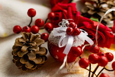 Yumuşak, beyaz bir battaniyede Noel süsleri. Toplar ve böğürtlen şeklinde kırmızı oyuncaklar, köknar kozalaklı. Sarı fenerlerin etrafında yıldızlar şeklinde ampuller var. Noel için zarif kompozisyon