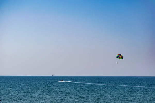 A rainbow-colored striped parachute with two passengers under it. People flying over the blue sea. Entertainment at the resort and active recreation on vacation and on vacation