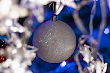 Noel ağacında ilginç Noel oyuncakları. Beyaz renkli Noel aksesuarları yanıp sönen fenerlerin ve ışıkların arasında. Aile tatilleri için şenlikli ve zarif şeyler..