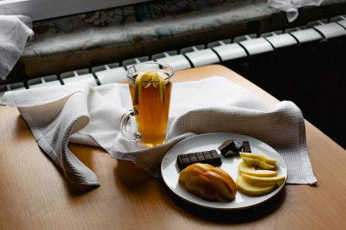 Şeffaf bir bardakta elma çayı, içecek, dilimlenmiş meyve ve çikolatanın yanında, sarı kabuklu taze elma dilimleri ile süslenmiş, her şey beyaz bir peçetenin üzerinde.