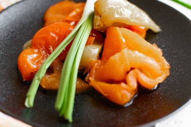 Tatlı dolmalık biber turşusu, dilimler halinde dilimler, siyah mat tabağında çok renkli sebzeler ve taş gibi beyaz bir arka plan. Tabak yeşil pırasalarla süslenmiş.