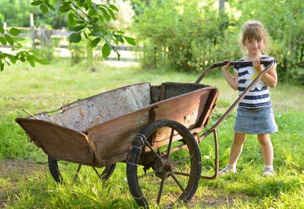 Little girl in striped t-shirt standing with old metal cart — Stock Photo, Image