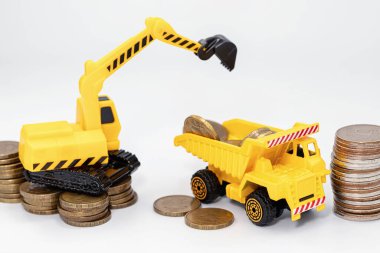 Oyuncak inşaat kazıcısı bir oyuncak kamyonun arkasına para yüklüyor.