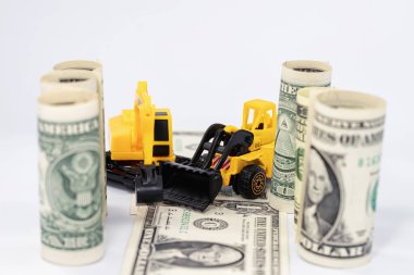 Sarı oyuncak buldozer dolar banknotlarından bir yol yapıyor.