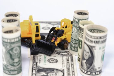 Sarı oyuncak buldozer dolar banknotlarından bir yol yapıyor.