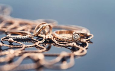 Üzerinde elmas ve altın zincir kolye olan altın bir yüzük koyu bir yansıtıcı yüzeyde duruyor.