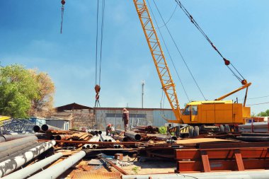 Depoda özel bir vinçle metal ürünleri ve boruları yüklüyorlar.
