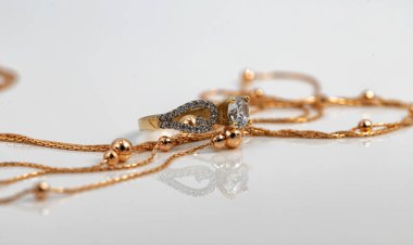 Altın boncuklu altın bir zincir ve büyük bir elmas yüzük beyaz yüzeye yansıyor.