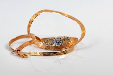 Yılan derisi örgülü altın bir zincir ve büyük bir elmas yüzük beyaz yüzeye yansıyor.