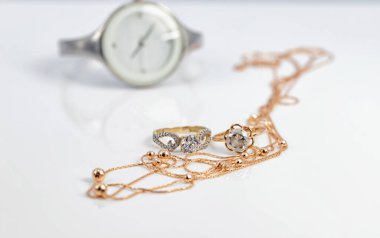 Altın elmas yüzükler ve boncuklu altın zincir beyaz bir kadının saatinin arka planında yatıyor.