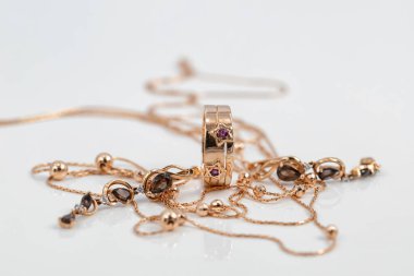 Yakut şeklinde yakutları olan altın bir yüzük, yakut küpeler ve beyaz yüzeye boncuklu altın bir zincir yansıtılır.