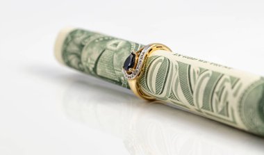 Altın bir safir yüzük bir dolarlık banknotun üstüne takılır ve bir boruya sarınır.