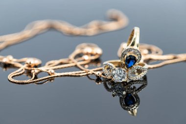 Topaz ve elmaslı iki zarif şekilli altın yüzük beyaz yüzeye yansıyor.