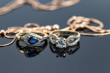 Topaz ve elmaslı iki zarif şekilli altın yüzük beyaz yüzeye yansıyor.