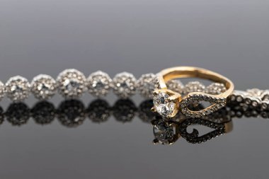 Elmas takılı zarif bir kadın yüzüğü değerli taşlı bir bileziğe takılır. Koyu arkaplan