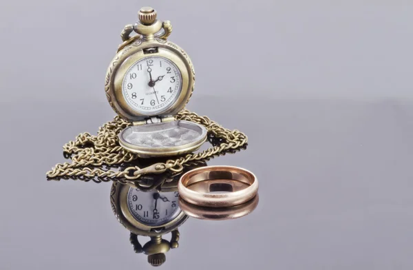 Pocket watch and a gold wedding ring on a reflective surface — Stock Photo, Image