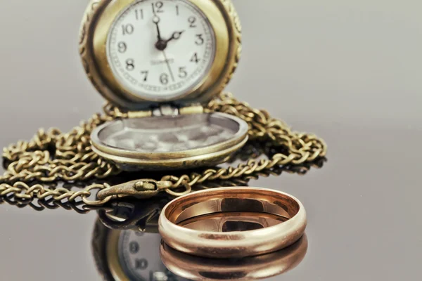 Reloj de bolsillo y un anillo de bodas de oro en una superficie reflectante — Foto de Stock