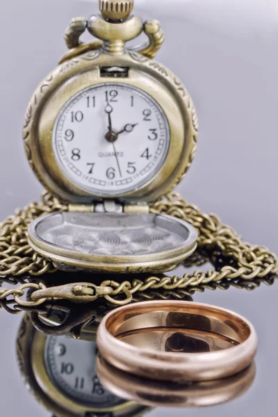 Карманные часы и золотое обручальное кольцо на отражающей поверхности — стоковое фото