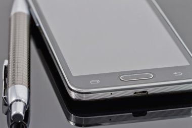 Yeni smartphone ve tükenmez kalem siyah bir yansıtıcı yüzey üzerinde yalan