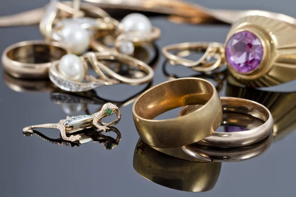 Gold wedding rings, earrings and chains on a reflective surface — Stock Photo, Image