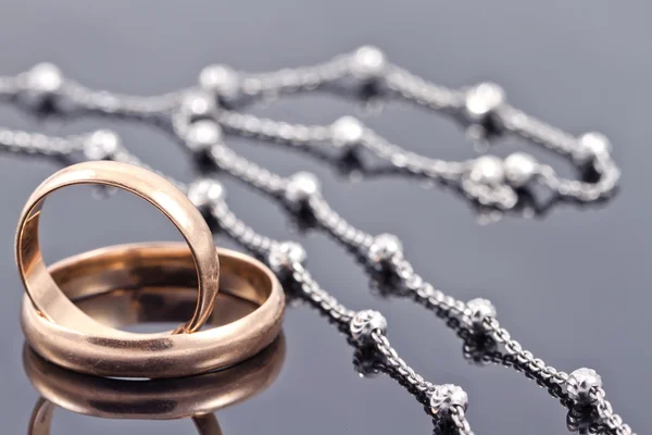 Anillos de boda dorados y elegante cadena de plata —  Fotos de Stock