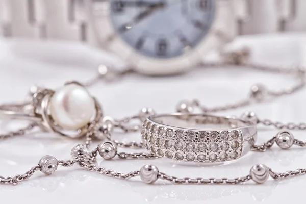 Серебряное кольцо и цепь на фоне часов — стоковое фото
