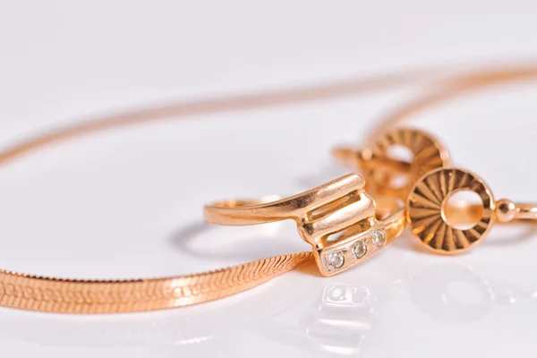 Elegant gold earrings and a ring from the same set amid gold snake chain weave — Stock Photo, Image